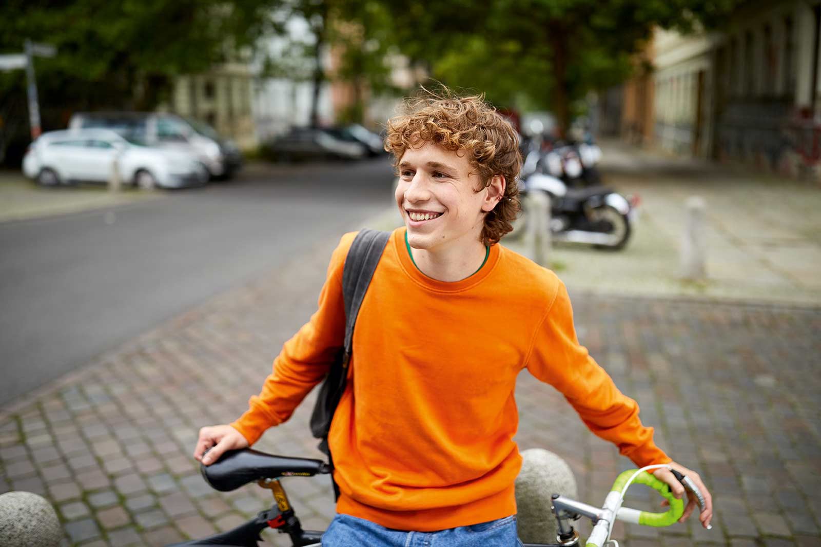 Ein jugendlicher Mann steht mit seinem Fahrrad auf einer Straße und lächelt