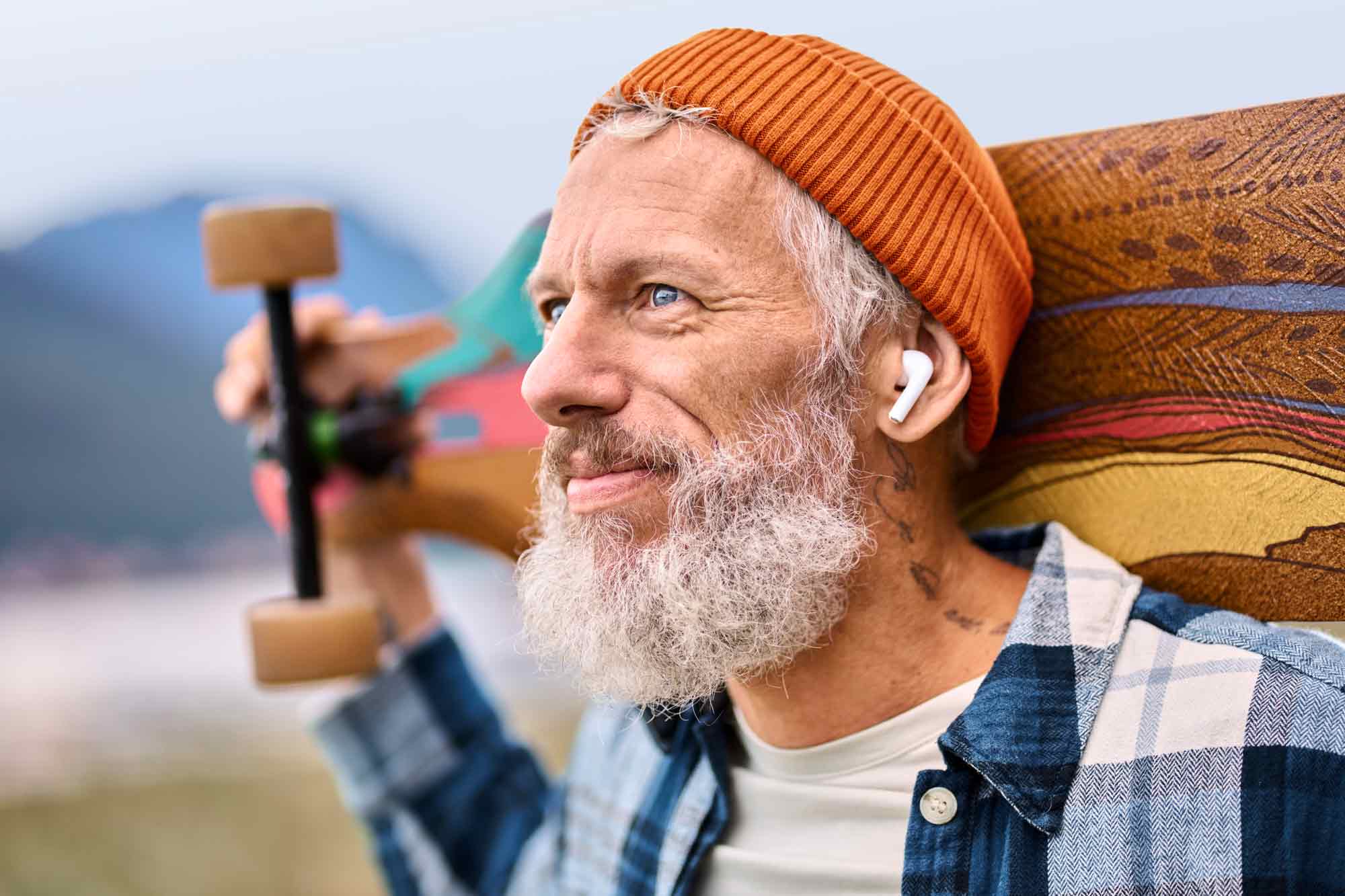 Ein mittelalter Mann mit Bart trägt sein Longboard und blickt selbstbewusst in die Zukunft