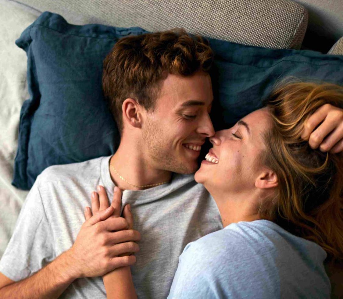 Ein junger Mann und eine junge Frau liegen auf dem Bett und lächeln