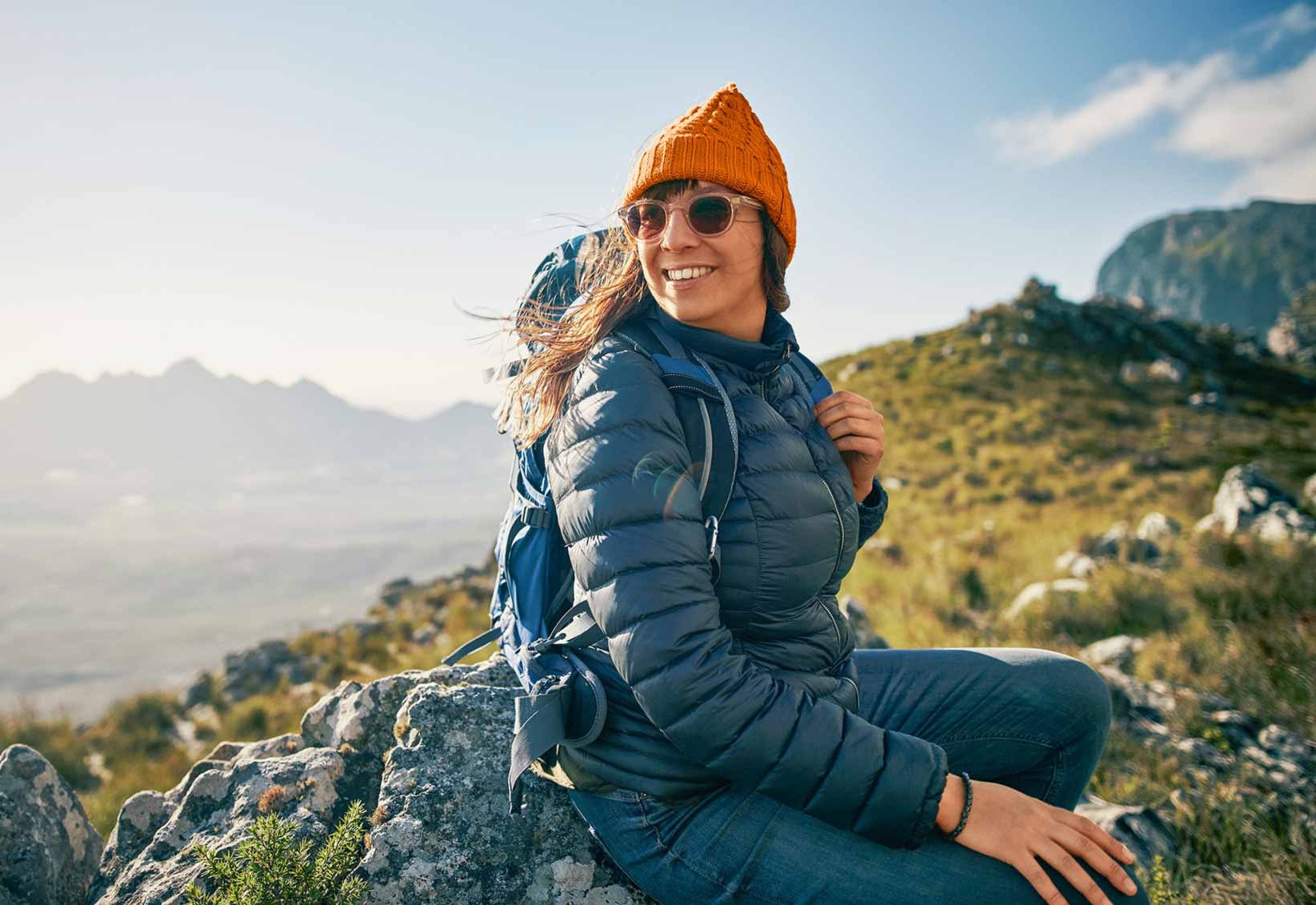 Eine junge Frau sitzt auf einem Berggipfel und lacht
