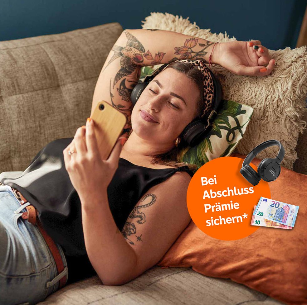 Junge Frau liegt entspannt auf dem Sofa und prüft ihre Geldanlage über ihr Smartphone