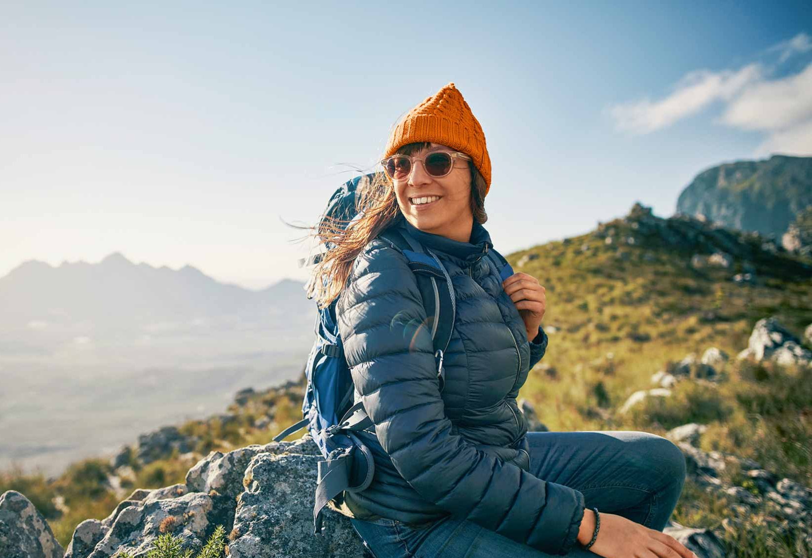 Eine junge Frau sitzt auf einem Berggipfel und lacht